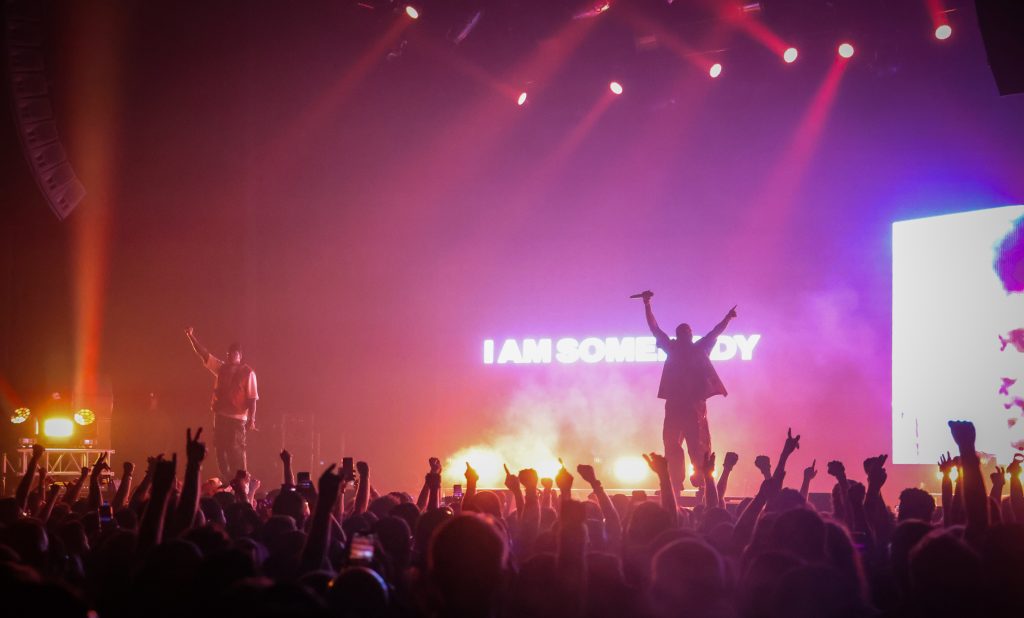 Clipse commanding the crowd on stage, with “I AM SOMEBODY” displayed on the LED screen.